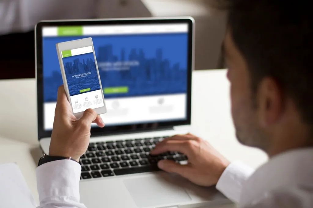 A man looking at a ebsite on his laptop and phone.